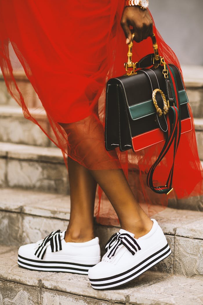 Elegant pose featuring modern sneakers and a chic designer handbag on stone steps.